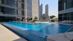 A swimming pool with a tiled edge, surrounded by modern buildings, and a clear sky. - Mesmerizing 2 Bed l Canal and Burj Views (Al Wasl)