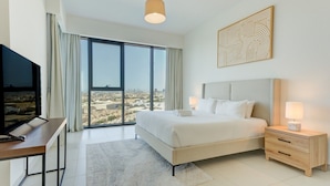A hotel room with a large bed, a desk with a TV, a nightstand with a lamp, and a city view through the window. - Mesmerizing 2 Bed l Canal and Burj Views (Al Wasl)