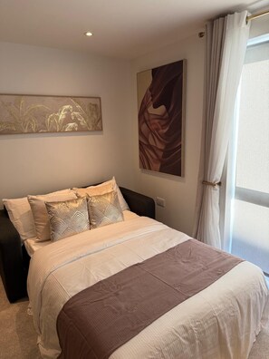 Una camera da letto con un letto, un comodino, un'opera d'arte appesa al muro e una finestra con tende.