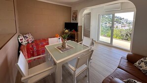 A room with a bed, a table with chairs, a TV, and a view through a large window. - Beautiful mountain apartment with sea views AV 91 (ROSES)