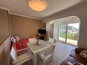 Ein Zimmer mit Bett, Tisch mit Stühlen, Fernseher und Blick durch ein großes Fenster.