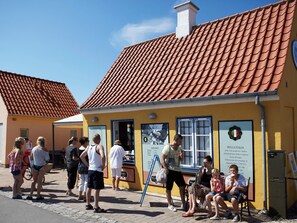 Ein gelbes Gebäude mit rotem Ziegeldach, einer Schautafel und einer Bank vor der Fassade.