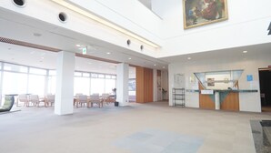 En rymlig entréhall med en receptionsdisk, sittgrupp och stora fönster.