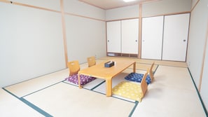 A tatami mat room with a low wooden table, chairs, and a traditional Japanese sliding door. - Sanzoku Hotel (Asago)