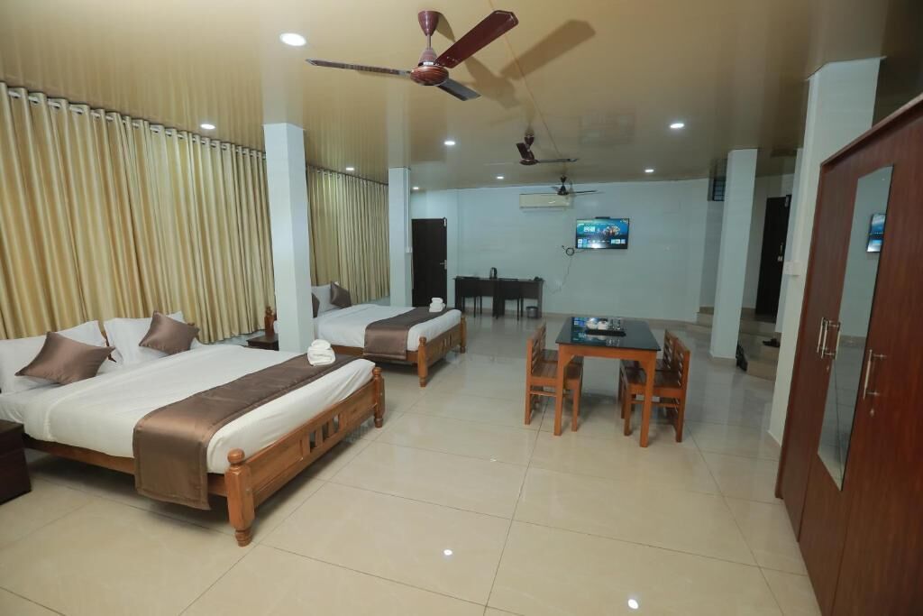 A hotel room with two beds, a dining table, chairs, a TV, and ceiling fans.