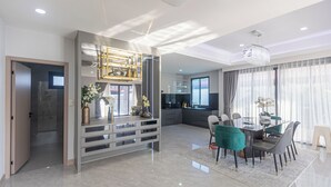 A modern interior with a dining area, kitchen, and a large window with curtains. - Spacious 5-bedroom house in charming Muang Pattaya C25 (Muang Pattaya)