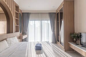 Ein modernes Hotelzimmer mit einem großen Bett, einem Fernseher, einem Schreibtisch und einem Kleiderschrank.