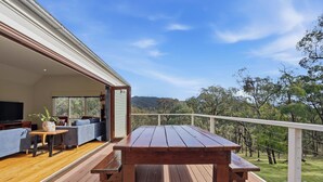 An outdoor deck with a wooden table and benches, a sofa, and a TV.