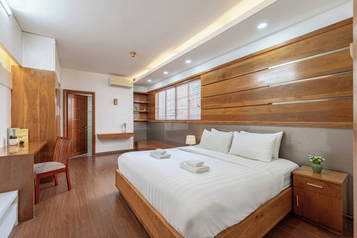 A modern bedroom with a wooden headboard, a bed with white linens, a bedside table, and a chair.