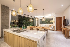 A modern kitchen with a marble island, wooden cabinets, and pendant lighting. - 4BR Private Pool Villa With Rice Views (Canggu)