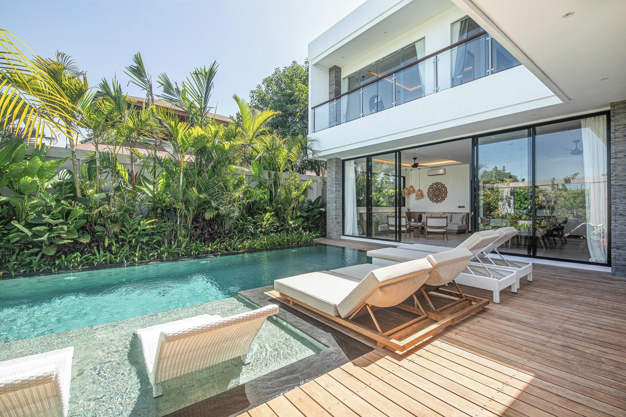 A modern house with a pool, lounge chairs, and tropical plants.