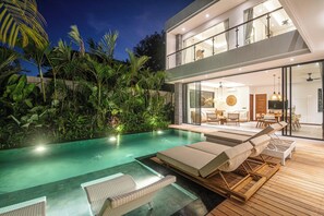 Une maison moderne dotée d’une piscine, de chaises longues et d’un espace repas.