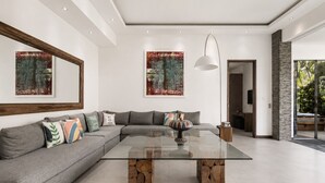 Un salon moderne avec un canapé d’angle, une table basse en verre aux pieds en bois et deux tableaux abstraits accrochés aux murs.