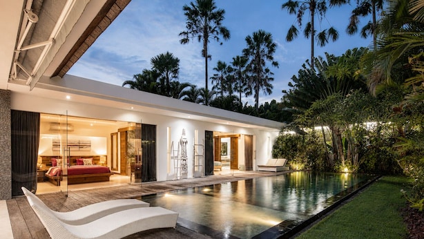 Une maison moderne dotée d’une piscine, d’une terrasse en bois et de plantes tropicales.