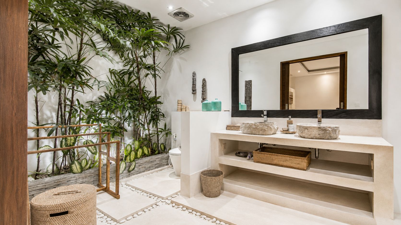 Un bagno con un ampio specchio, un lavabo a due vasche, uno scaffale in legno e una parete ricca di piante.