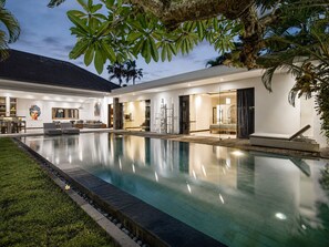A modern house with a swimming pool, a dining area, and a living room with a sofa and a TV. - Elegant 3BR Oasis in the Heart of Seminyak (Seminyak)