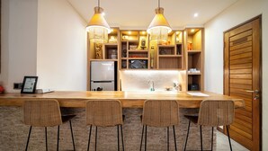 A kitchen with a wooden island, bar stools, pendant lights, and built-in shelves. - Canggu Coastal Living: 4BR Villa Near Finns (Canggu)