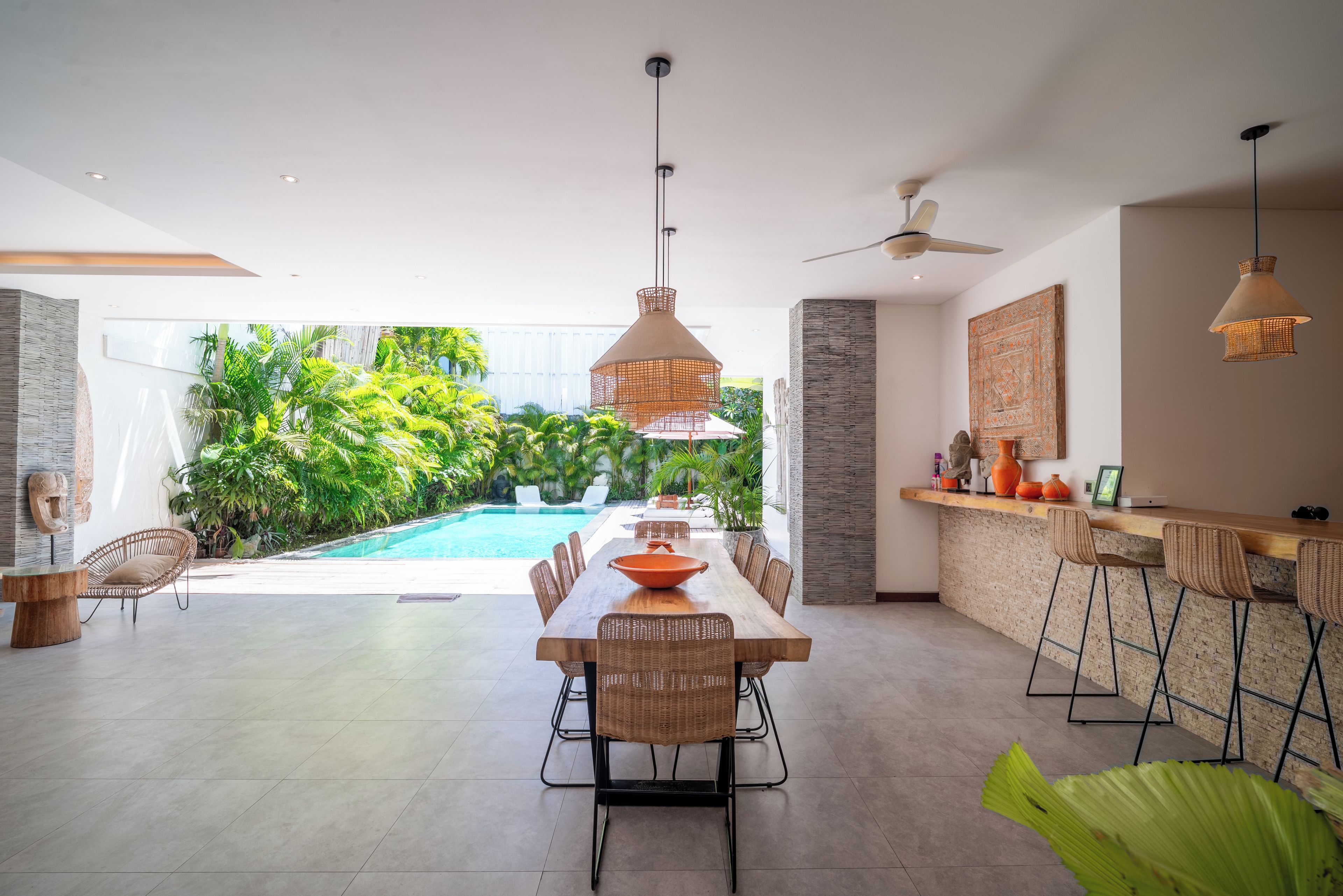 A modern dining area with a pool view, wicker furniture, and a bar with stools.