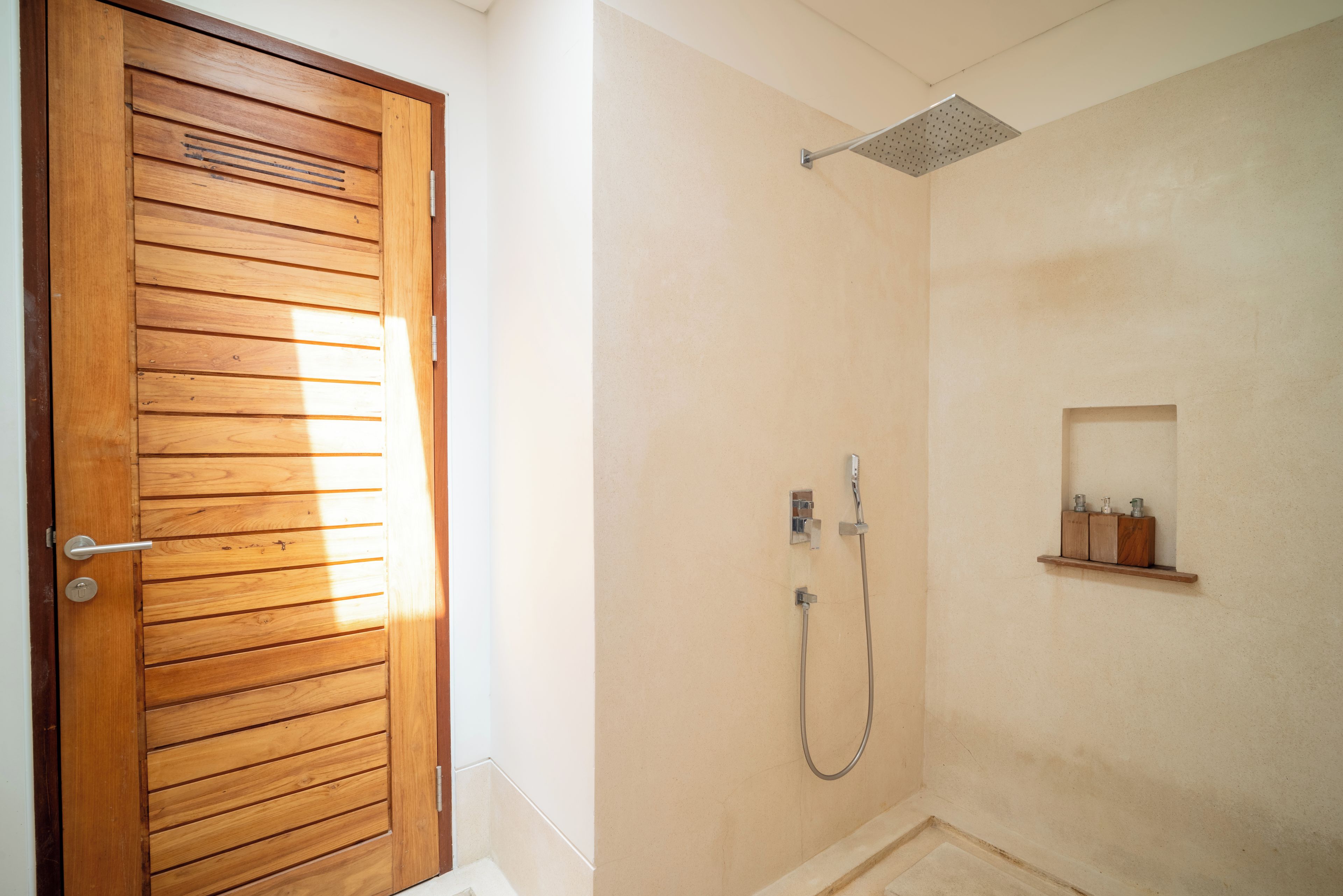 Bagno con porta in legno, doccia e ripiano con articoli da toilette.