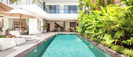 Ein modernes Haus mit Swimmingpool, Gartenmöbeln und üppiger Bepflanzung.