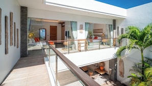 A modern interior with a glass balcony, a seating area with cushions, and a wooden floor. - Canggu Coastal Living: 4BR Villa Near Finns (Canggu)