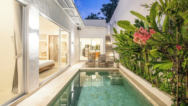 Ein moderner Poolbereich mit Glasveranda, Essbereich mit Außenmöbeln und üppiger Bepflanzung.