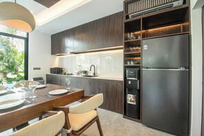 Une cuisine moderne avec des meubles de couleur bois foncé, un réfrigérateur encastré et un coin repas comprenant une table et des chaises en bois.