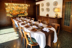 Ein Esszimmer mit einem langen Tisch, der für eine Mahlzeit gedeckt ist, Holzsesseln, einem Kronleuchter und einer Wand mit dekorativen Tellern.