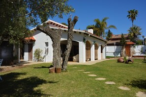 A white building with a red-tiled roof, arched doorways, and a well-maintained lawn with stone steps leading to the entrance. - 15 min. drive from Sitges Villa El Ranch 10 min. walk to the beach Jacuzzi 12P (Sitges)
