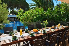 A dining table set outdoors with chairs, a pool in the background, and greenery. - 15 min. drive from Sitges Villa El Ranch 10 min. walk to the beach Jacuzzi 12P (Sitges)