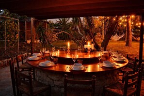 Ein Essbereich im Freien mit einem runden Tisch, gedeckt für eine Mahlzeit, umgeben von Stühlen, Kerzen und Lichterketten.