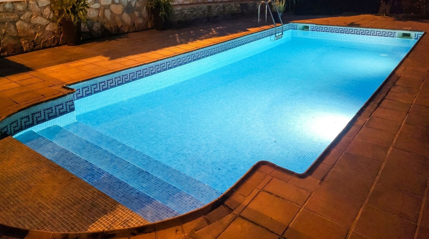 Una piscina rectangular con borde de azulejos, rodeada por un muro de piedra y un deck también de azulejos.