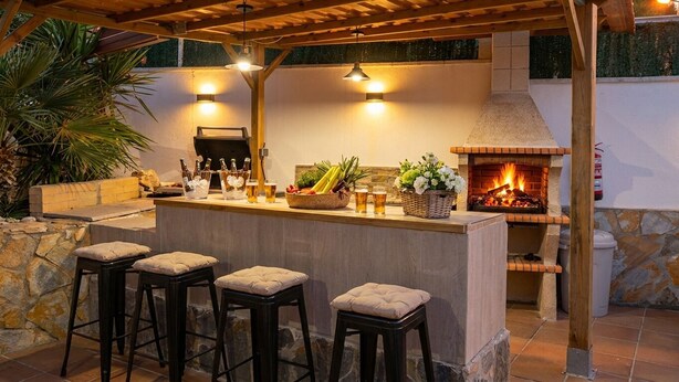 An outdoor bar area with a stone wall, a brick oven, and three stools.
