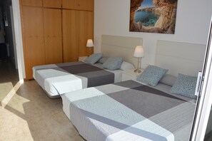 Ein Schlafzimmer mit zwei Betten, einem Holzschrank, einem Bild einer Küstenlandschaft und einem Fliesenboden.