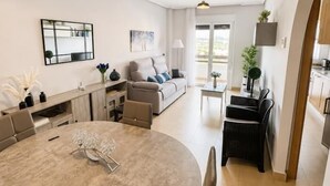 Ein modernes Wohnzimmer mit einem runden Esstisch, einer Couch, einem Couchtisch und einem durch eine offene Tür einsehbaren Küchenbereich.