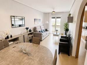 Ein modernes Wohnzimmer mit einem runden Esstisch, einer Couch, einem Couchtisch und einem durch eine offene Tür einsehbaren Küchenbereich.