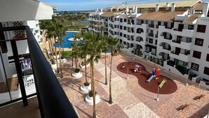 Ein Hotelinnenhof mit Pool, Palmen und einem Spielplatz.