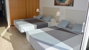 Ein Schlafzimmer mit zwei Betten, einem Holzschrank, einem Bild einer Küstenlandschaft und einem Fliesenboden.