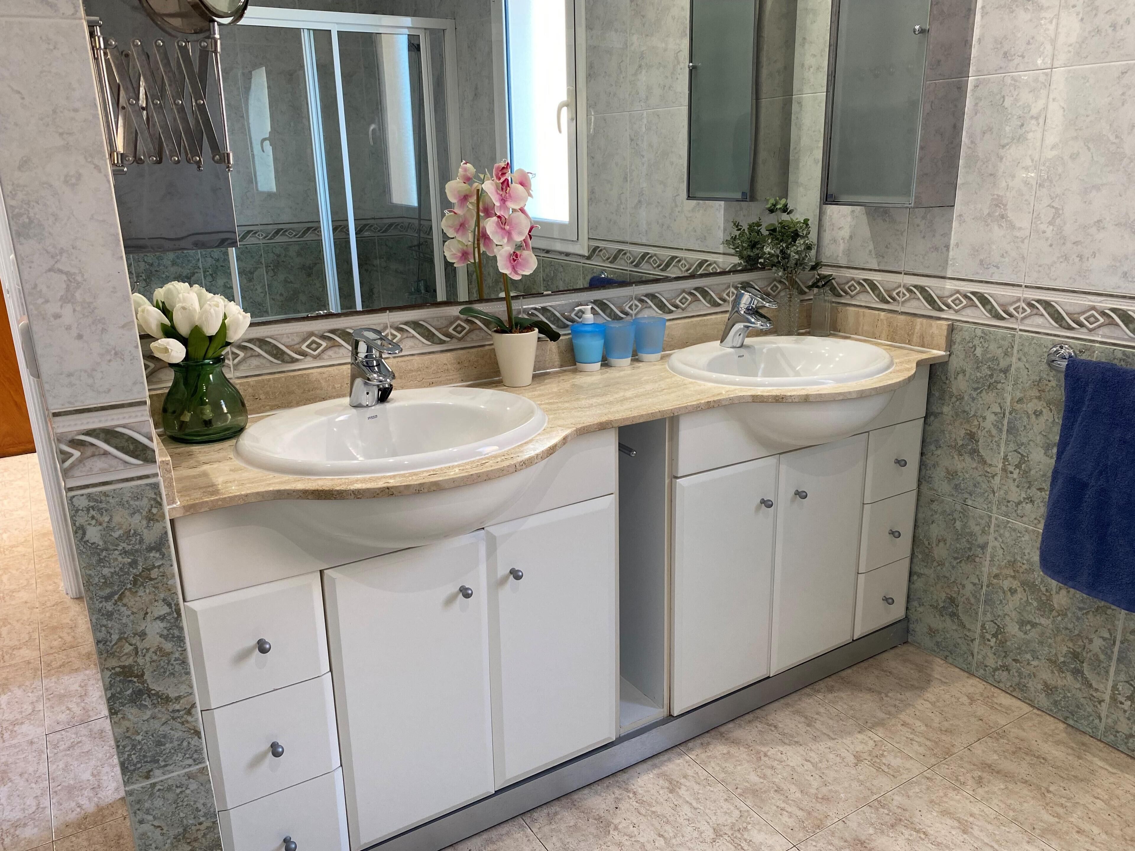 A bathroom with two sinks, a mirror, cabinets, and a blue towel.