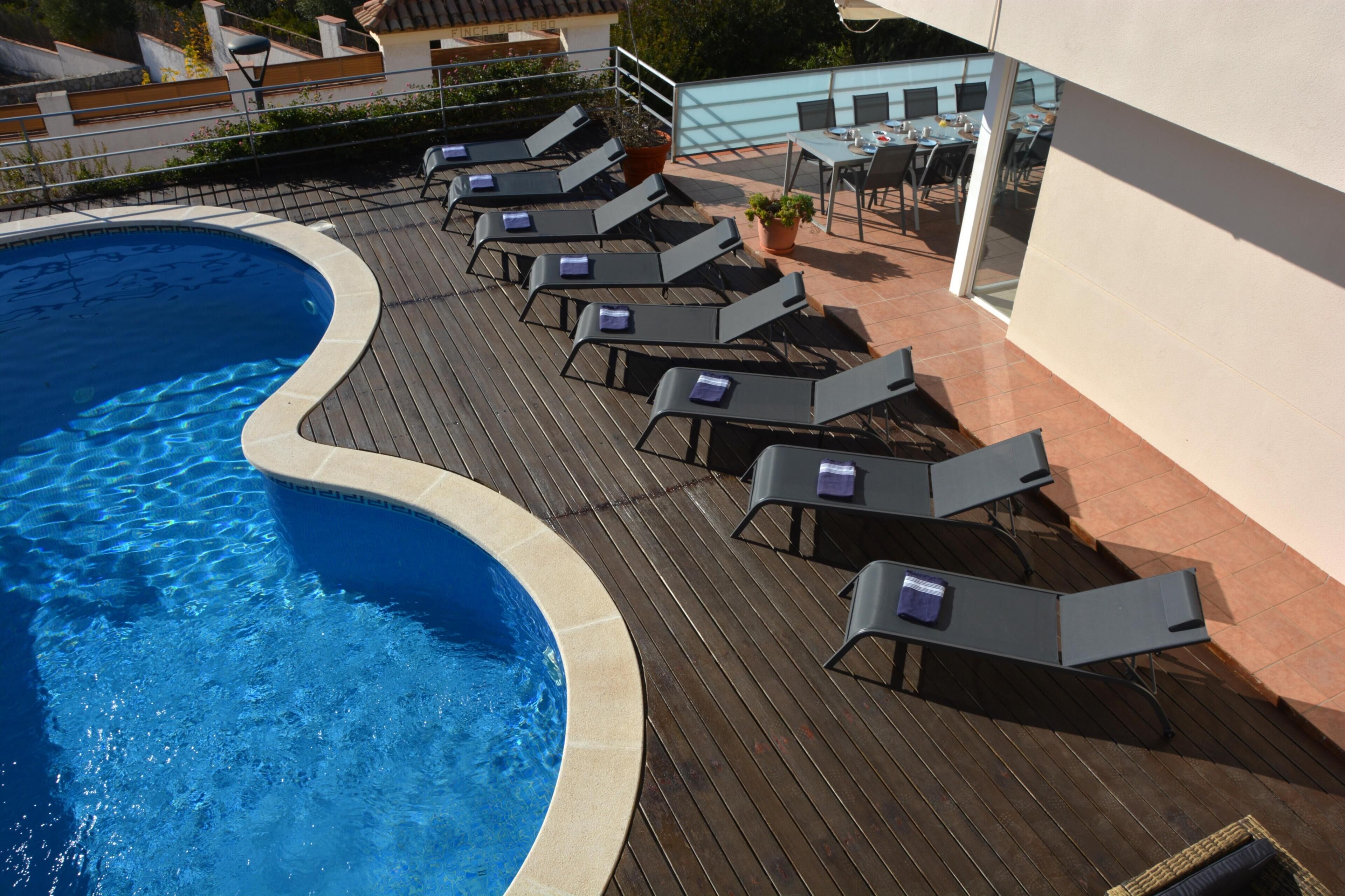 A swimming pool with lounge chairs and a table, surrounded by a wooden deck and a building.