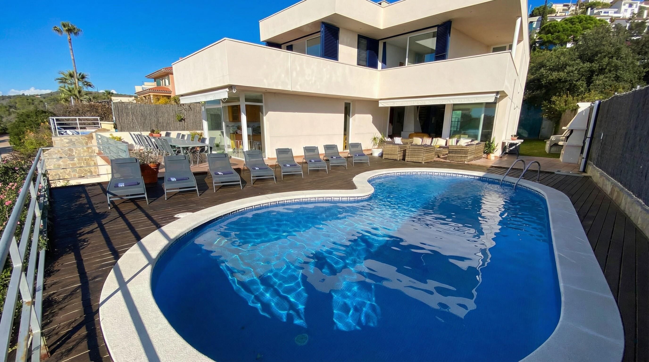 A modern building with a swimming pool, lounge chairs, and a stone wall.