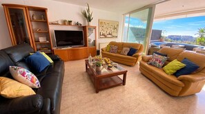Ein Wohnzimmer mit einer schwarzen Ledersofa, einer braunen Ledersofa und einem Glastisch. Ein Fernseher steht auf einer Holzkommode, und ein Gemälde hängt an der Wand.