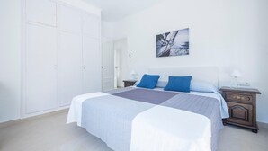 Une chambre à coucher comprenant un lit, deux tables de chevet, une armoire en bois et un tableau accroché au mur.