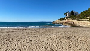 A beach with a white building on a cliff, clear blue sky, and calm sea. - Villa Playa del Sur · 250m from the sea · 7 Suites · +19 guests · Views 10 P (Capafonts)
