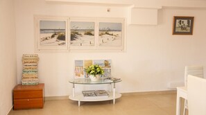 Een kamer met een glazen tafel, een houten kast en een wand met ingelijste kunstwerken.