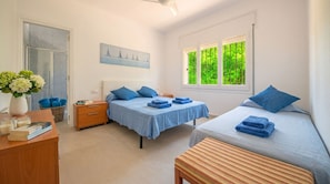 Een slaapkamer met twee bedden, een nachtkastje, een raam met uitzicht op groen en een schilderij aan de muur.