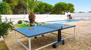 Ein Tischtennis-Tisch im Freien, im Hintergrund ein Schwimmbecken.