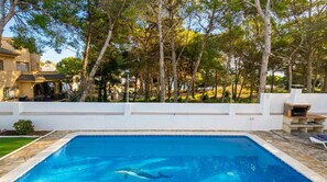 Schwimmbecken mit einem Delfin, umgeben von Bäumen und einer weißen Mauer.