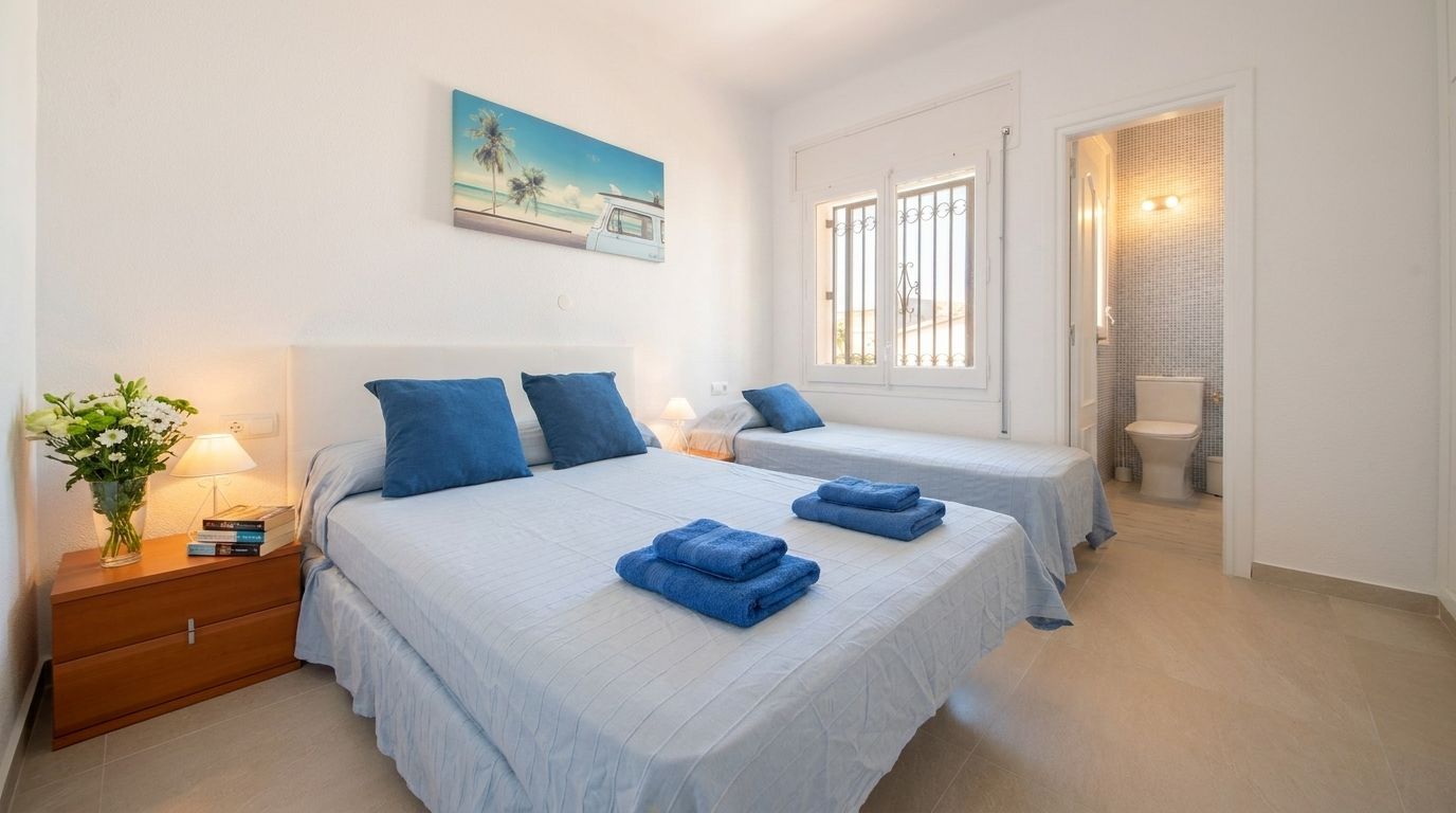 A bedroom with two beds, a nightstand, a bedside table with a lamp, a painting on the wall, and a bathroom visible through an open door.