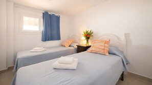 A hotel room with two beds, a window with curtains, a bedside table with a lamp and flowers, and a wall-mounted light fixture. - Villa Playa del Sur · 250m from the sea · 7 Suites · +19 guests  · Views 14 P (Capafonts)